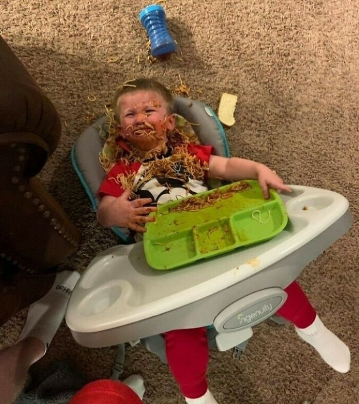 Child covered in spaghetti, sitting in a high chair; bizarre and eclectic scene.