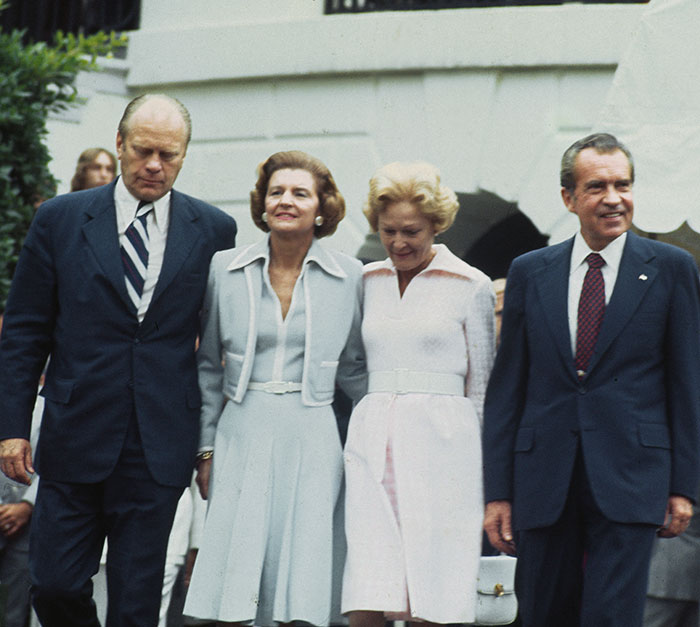 "Past first ladies in formal dresses, walking with presidents at an event, highlighting style comparisons."