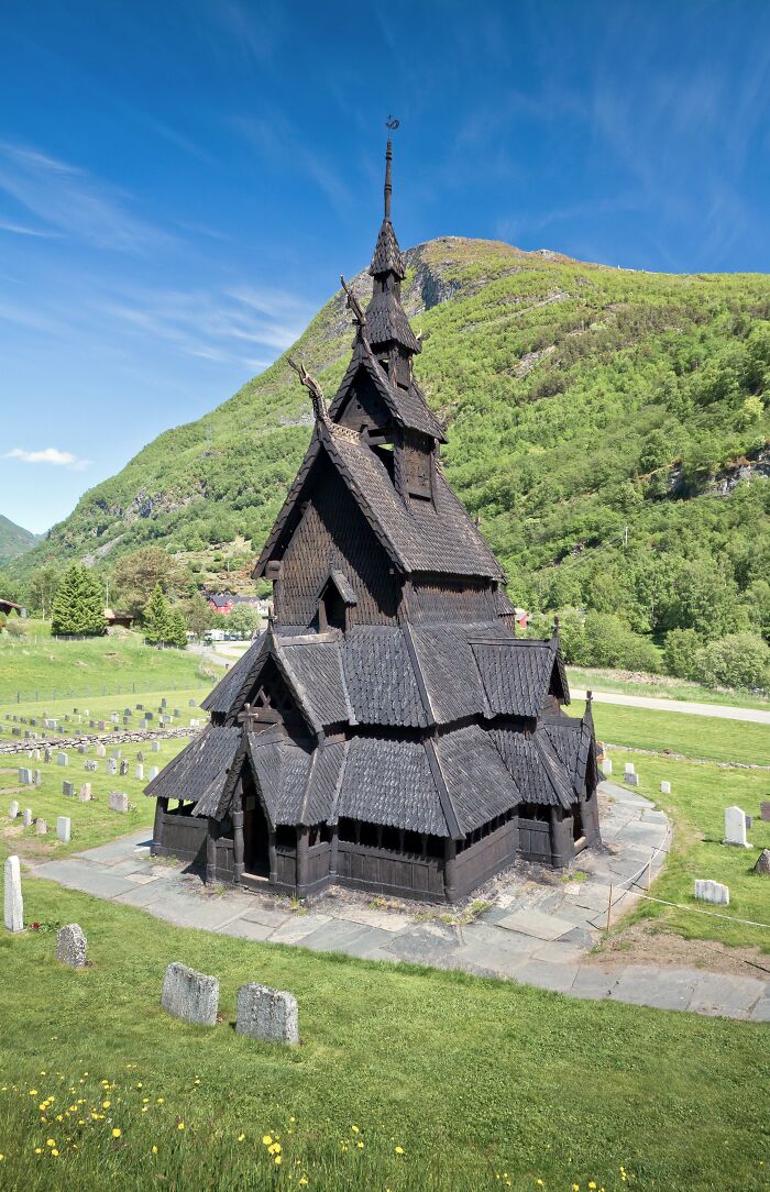 Historic wooden church amid lush green landscape under a bright blue sky, showcasing stunning architecture.