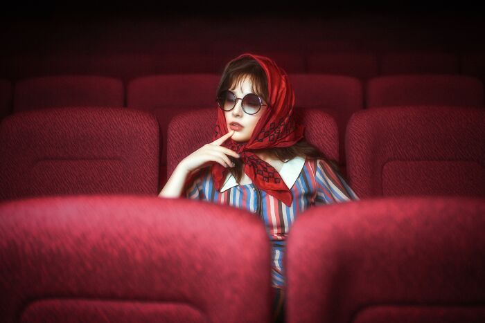 Person in a red scarf and sunglasses sitting in a theater, depicting Budapest International Foto Awards winners.