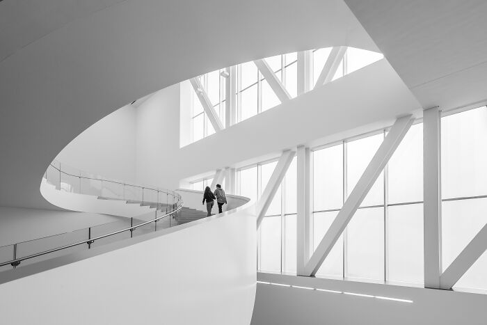 Two people walking on a curved ramp in a modern building, a winner from the Budapest International Foto Awards 2024.