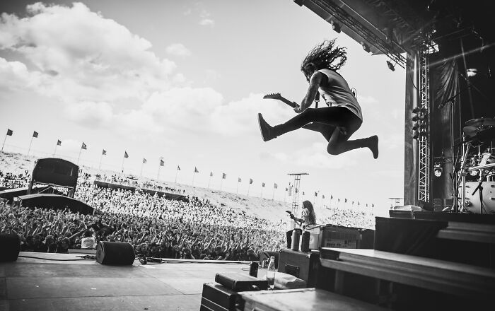 Guitarist in mid-air jump on stage at Budapest International Foto Awards, with a large crowd in the background.