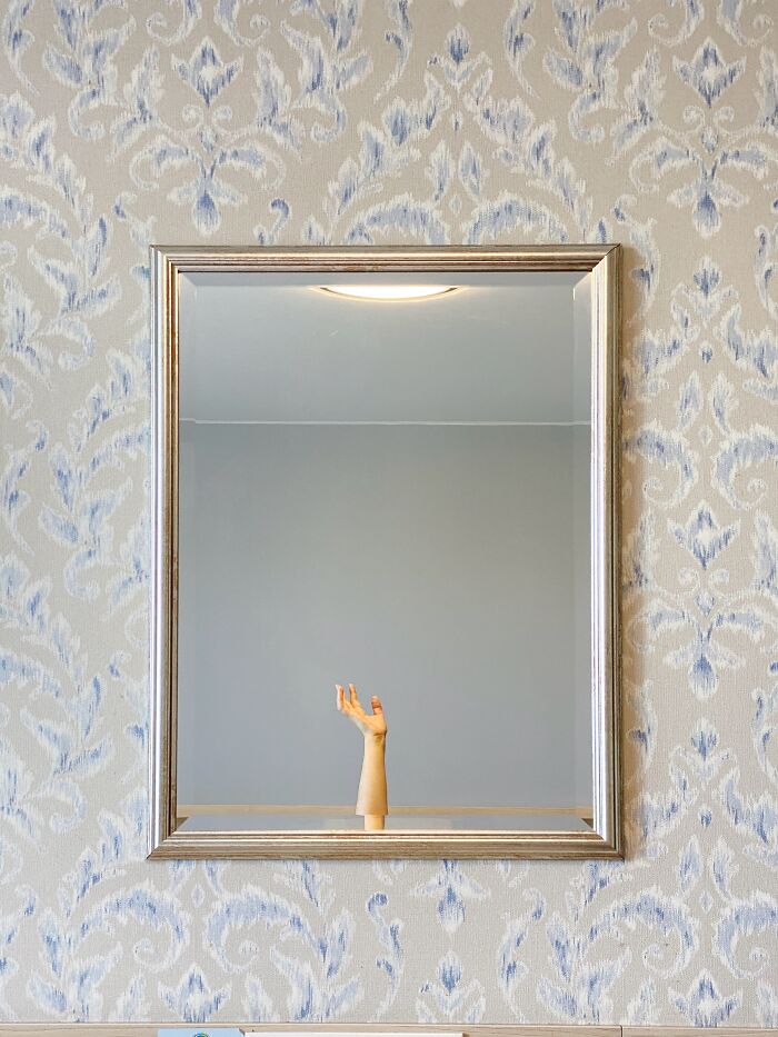 Framed mirror on patterned wall reflecting a mannequin hand, featured in Budapest International Foto Awards.