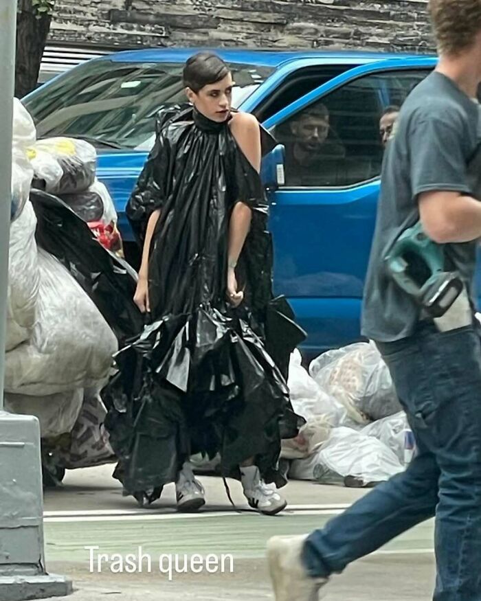 NYC local in experimental fashion outfit resembling a gown made from black garbage bags, walking on a city street.