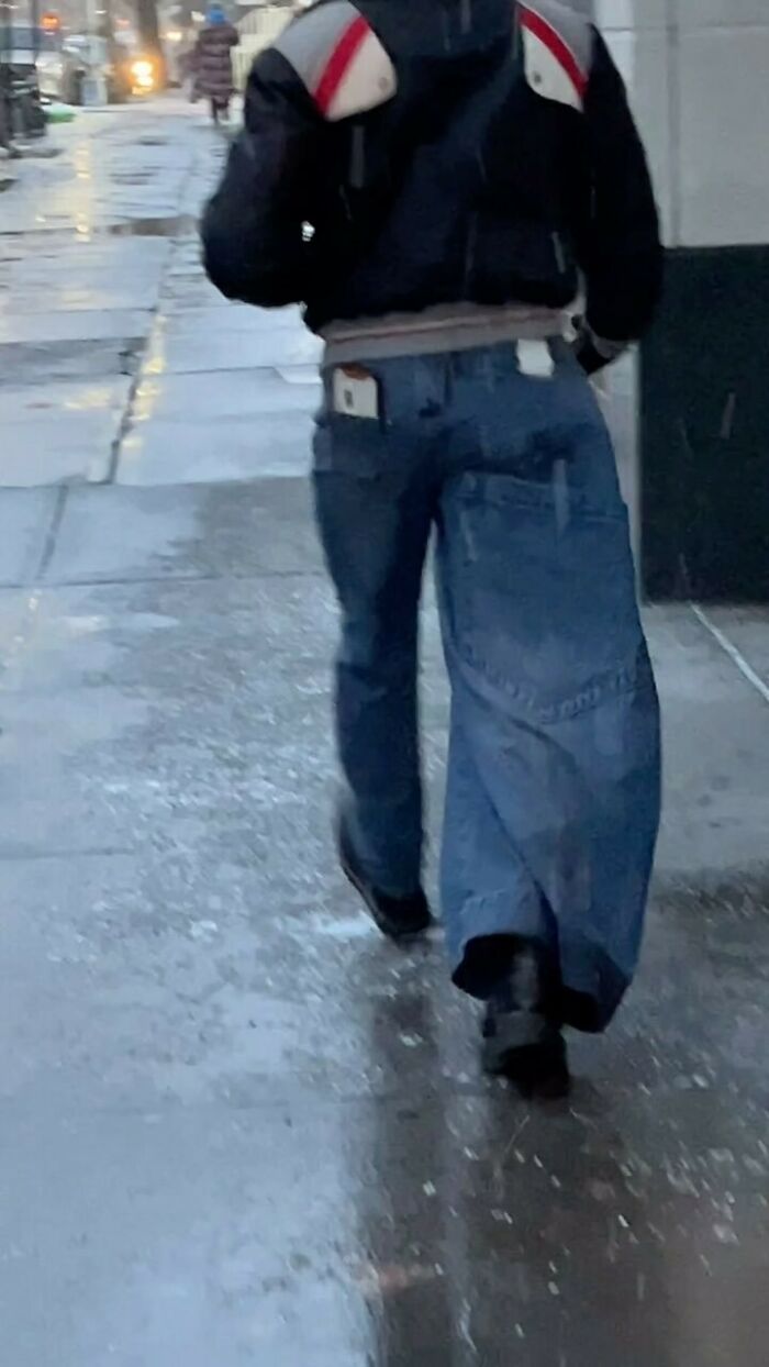 New York local in oversized jeans and a jacket, showcasing experimental fashion on a rainy city sidewalk.