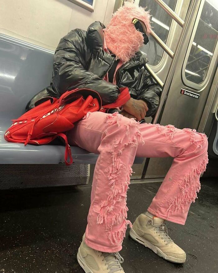 NYC local in vibrant pink, textured fashion on the subway, showcasing experimental street style with red backpack.