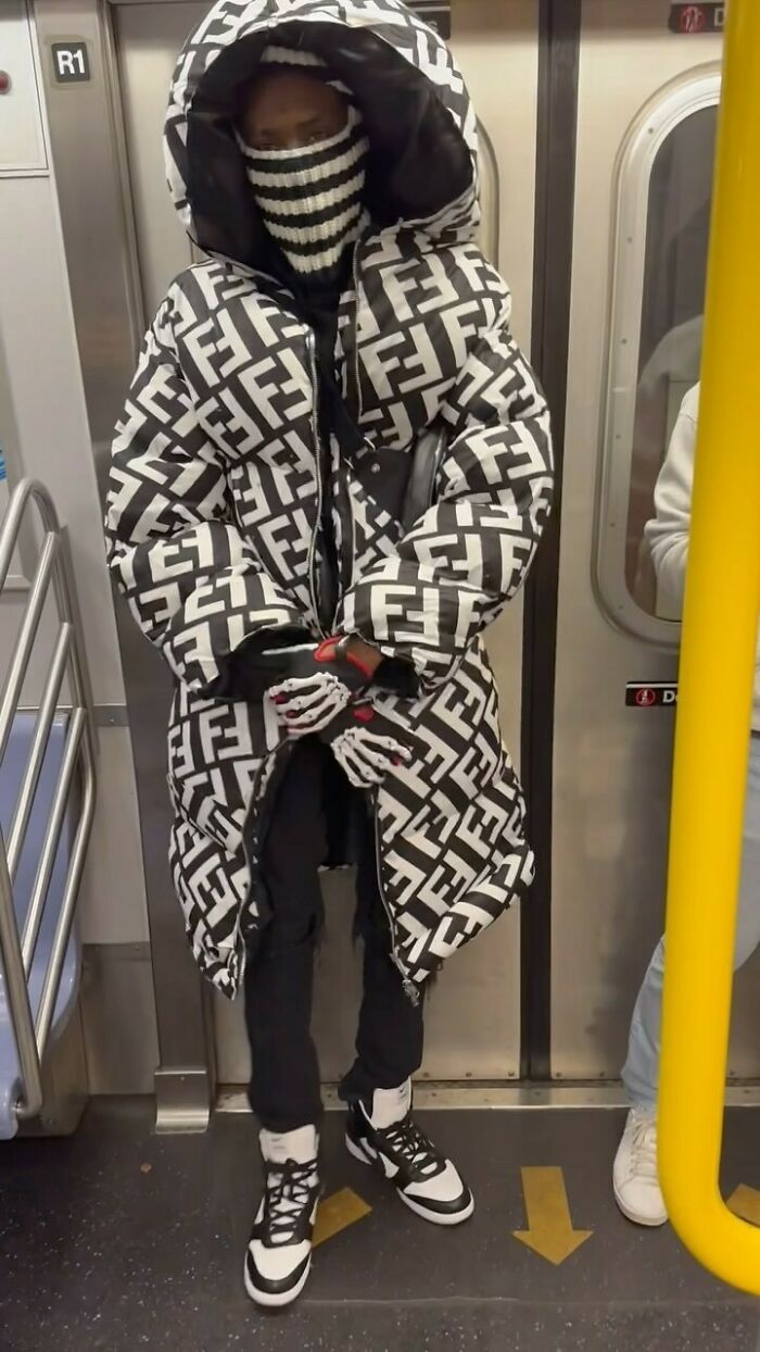 New York local on subway in bold, geometric patterned coat and striped mask, showcasing experimental fashion.