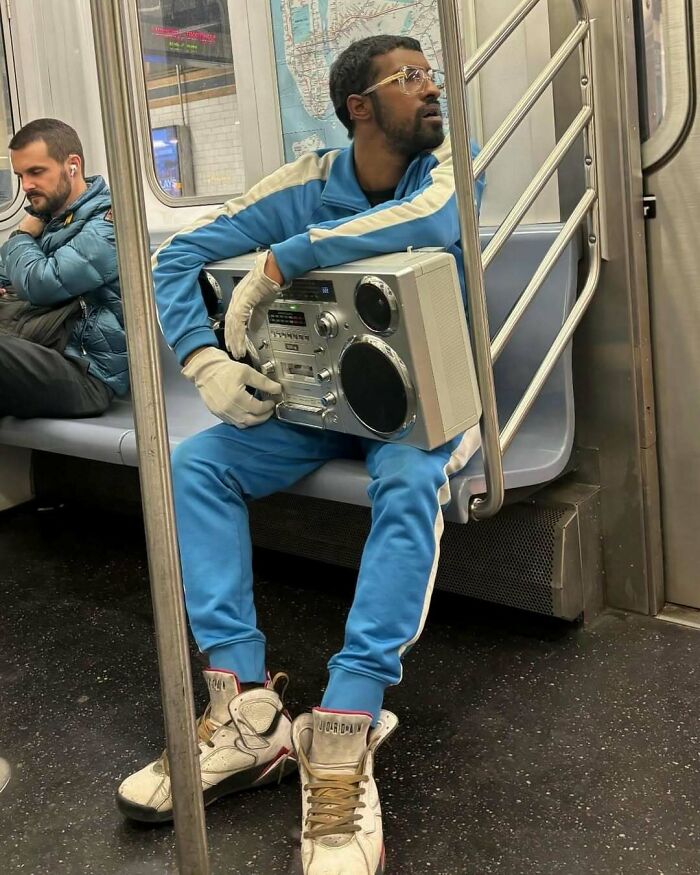 Man on NYC subway in a blue tracksuit with a retro boombox, showcasing unique New York fashion.