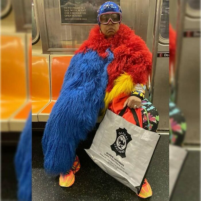 New York local in colorful, experimental fashion on the subway, wearing vibrant furry coat and holding a shopping bag.