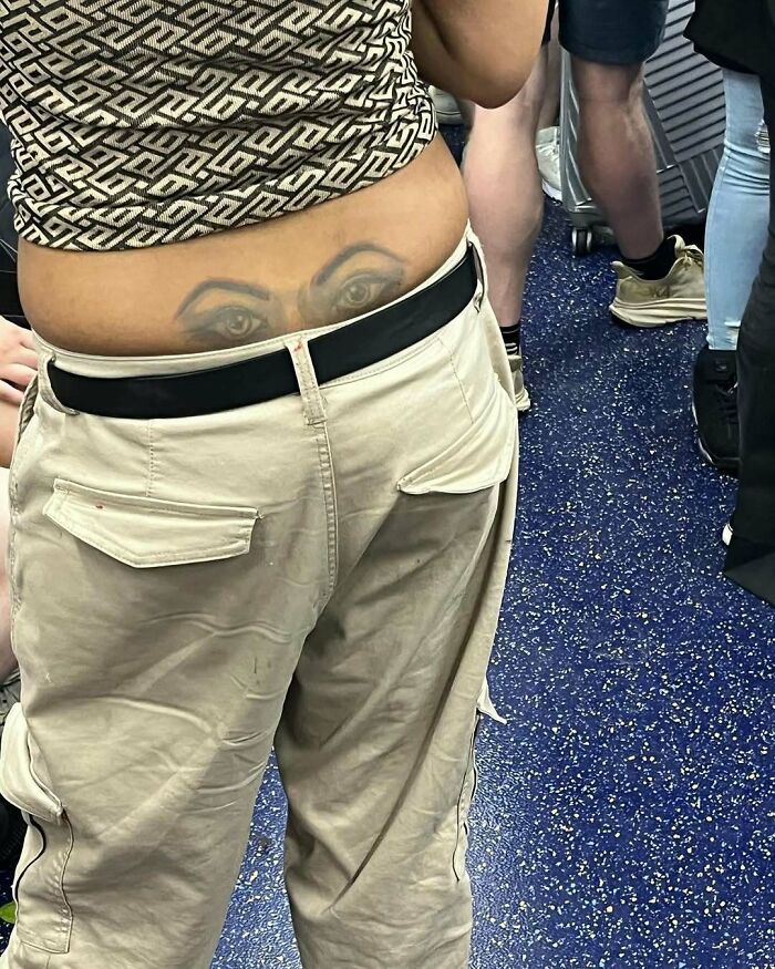 A subway passenger with a tattoo of eyes on their lower back.