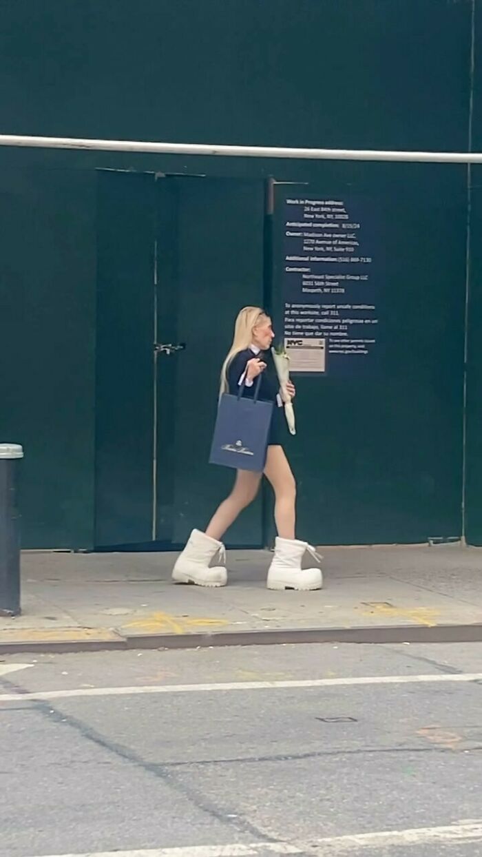 NYC local in daring fashion, wearing oversized white boots, walking with a tote bag and flowers.