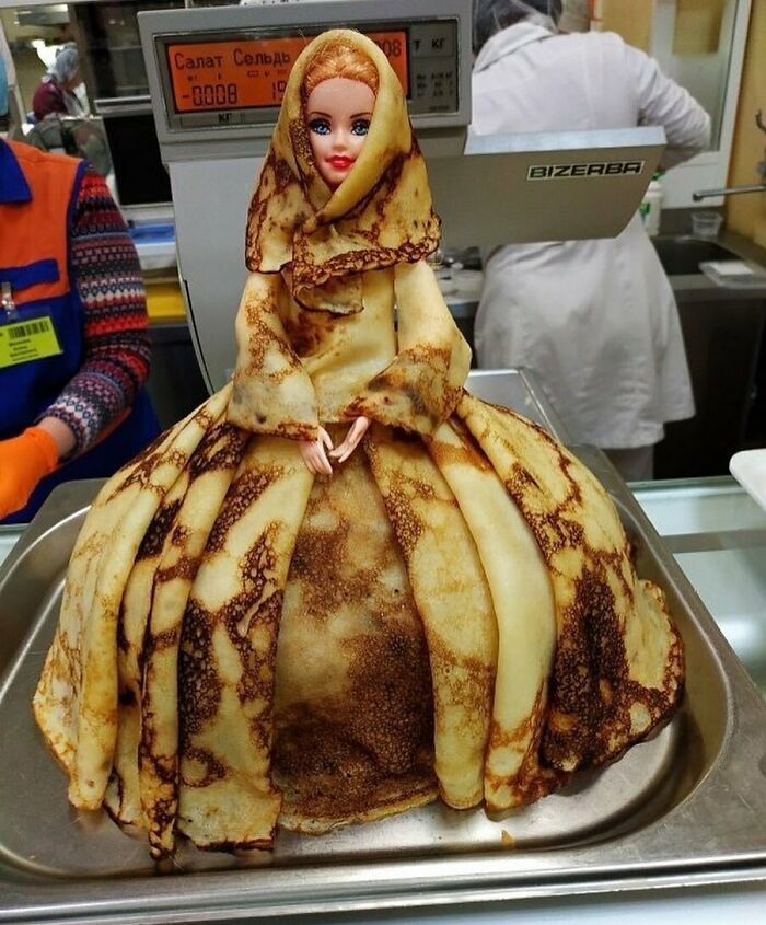 Toy doll wrapped in pancake layers, resembling a dress, displayed on a tray, showcasing bizarre eclectic creativity.