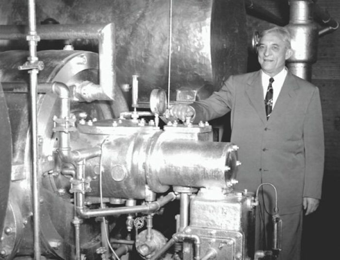 Man in suit standing beside a vintage industrial machine, showcasing a historical invention ahead of its time.