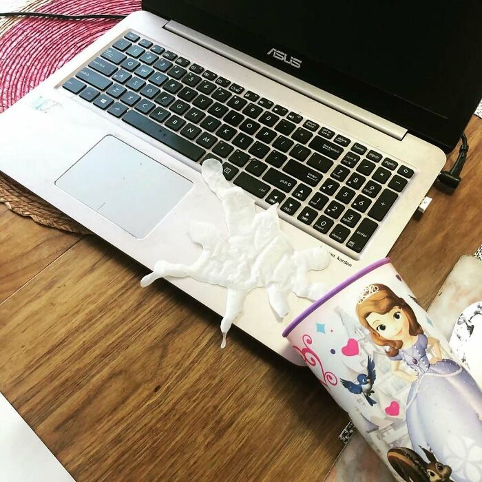 Kids' spilled drink on a laptop with a princess cup nearby, creating a humorous mess.