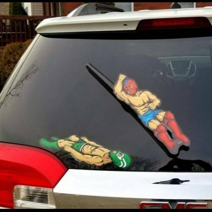 Car window with bizarre wrestling-themed wiper stickers.