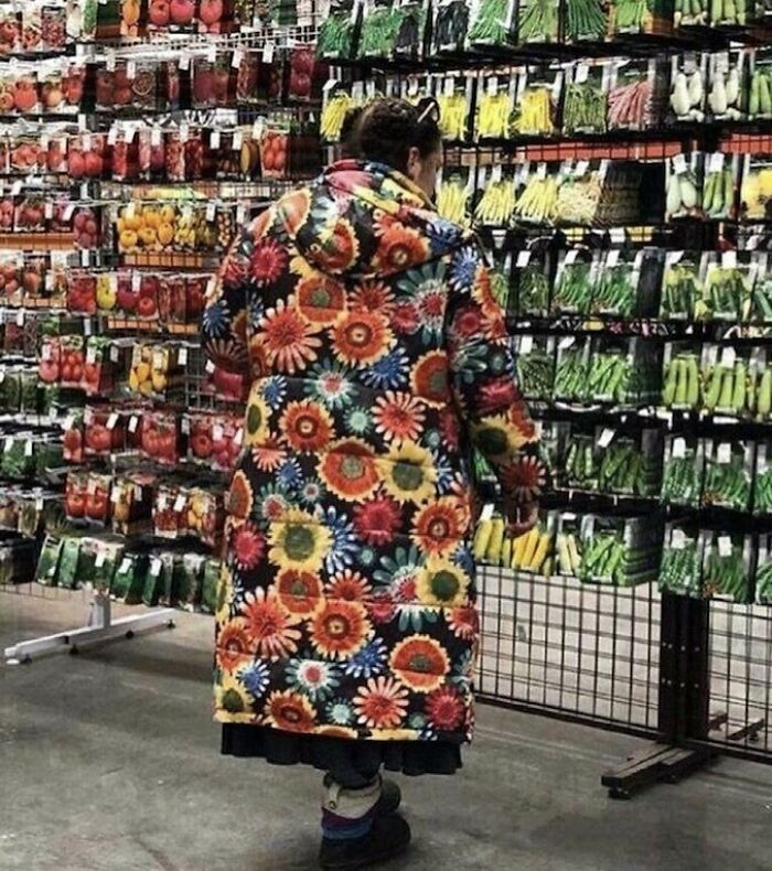 Person in a colorful flower-patterned coat browsing seed packets, embodying bizarre fashion in an eclectic setting.