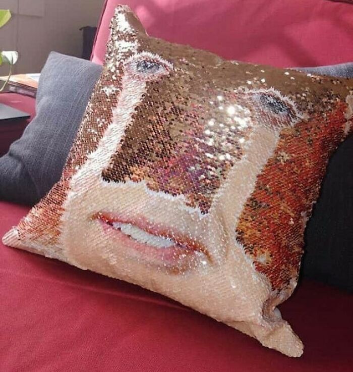 Sequin pillow with a distorted face design, adding bizarre charm to a red couch.