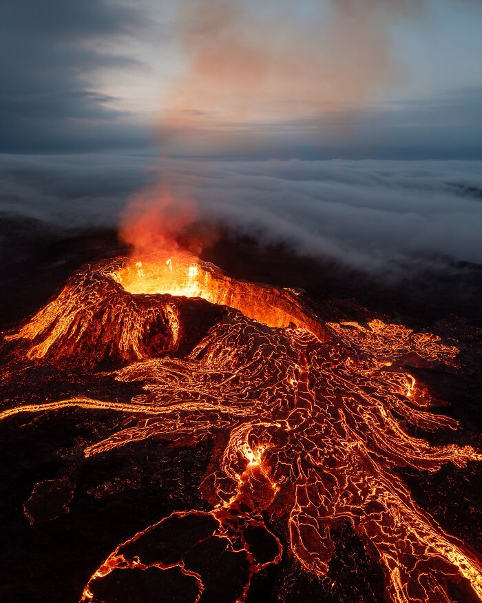 Aerial view of an active volcano with glowing lava flows under a cloudy evening sky, capturing the untamed nature.