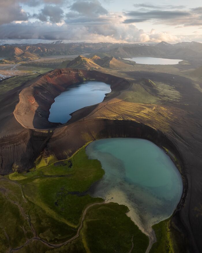 Aerial view of volcanic craters filled with blue lakes surrounded by lush green fields in untamed nature.