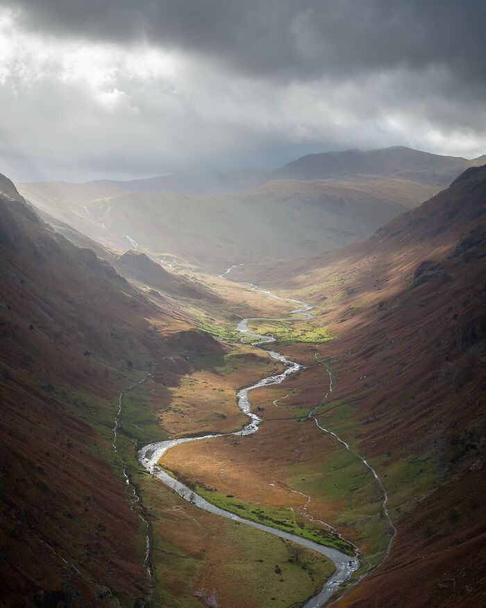 A winding river through a rugged valley, capturing untamed nature with dramatic clouds and lighting.