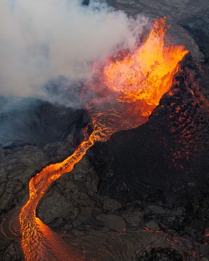 Aerial view of an erupting volcano with flowing lava and smoke, capturing untamed nature's fiery scene.