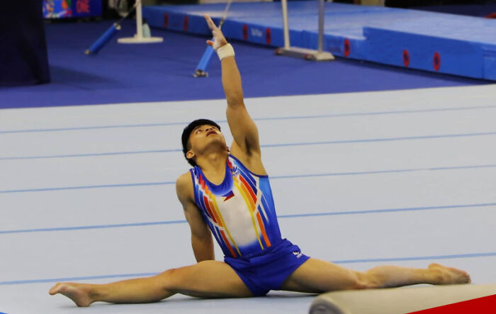 Gymnast performing a floor routine in colorful attire at an event, showcasing flexibility and athletic skill.