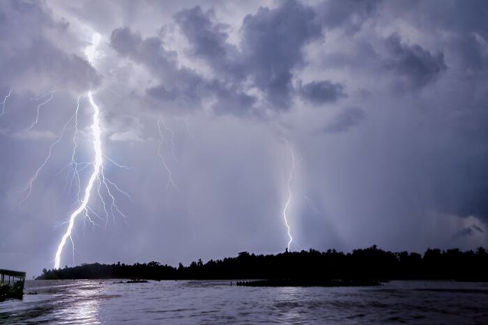 Lightning striking over a body of water, showcasing a stunning natural phenomenon under a cloudy night sky.