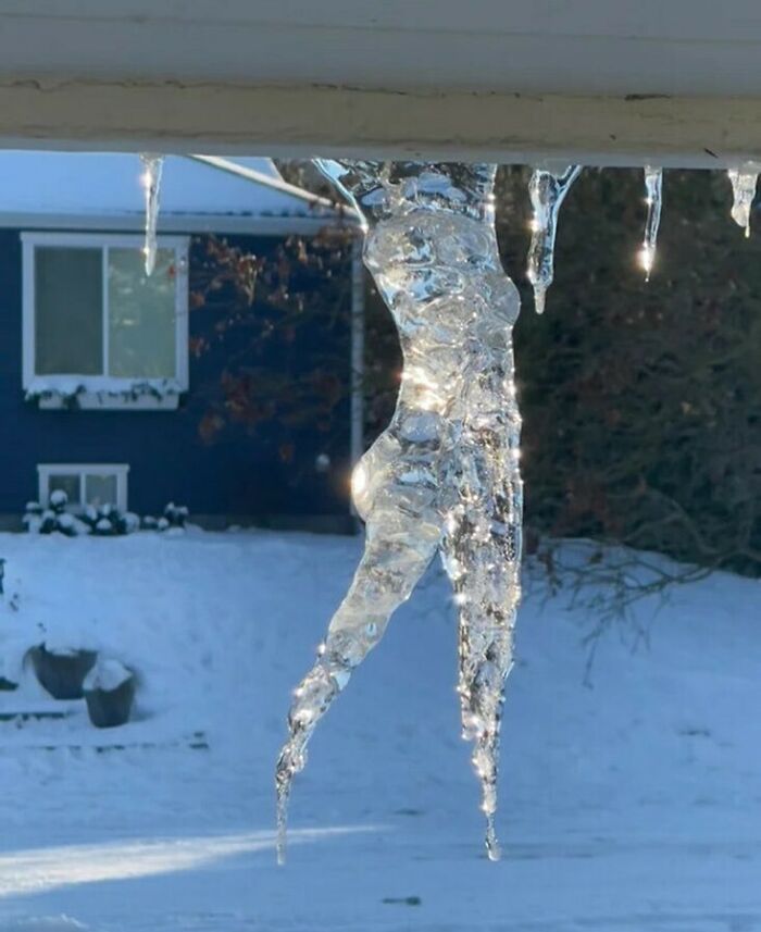 Icicle shaped like a dancer hanging from a roof, highlighting bizarre winter scene.