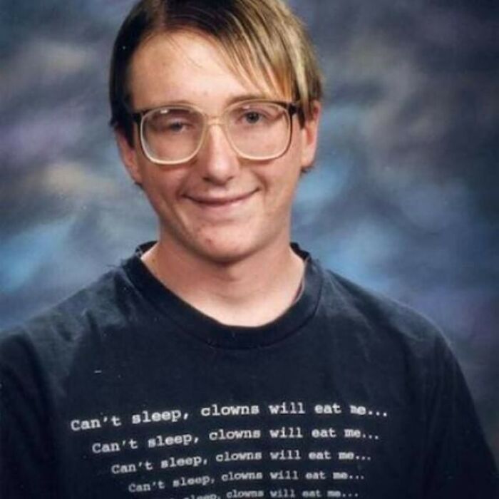 Person with glasses wearing a quirky "Can't sleep, clowns will eat me" shirt, showcasing bizarre humor.