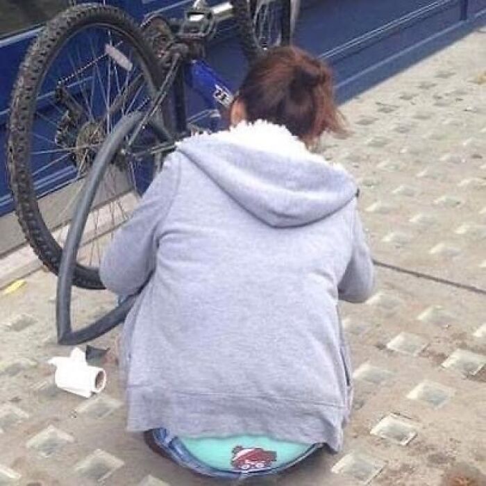 Person fixing bike tire on sidewalk, unusual scene from eclectic Instagram page.