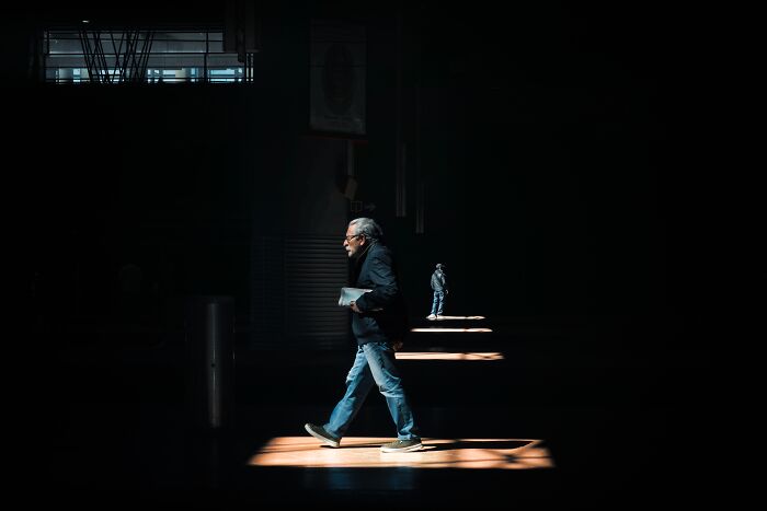 Man walking through a sunlit area in a shadowed room, representing entry for Tokyo Foto Awards 2024.