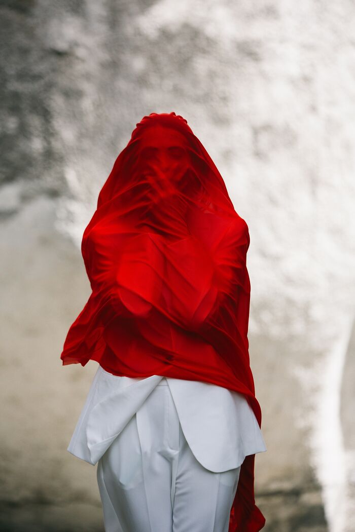 Person draped in red fabric against a textured background, featured in Tokyo International Foto Awards exhibit.