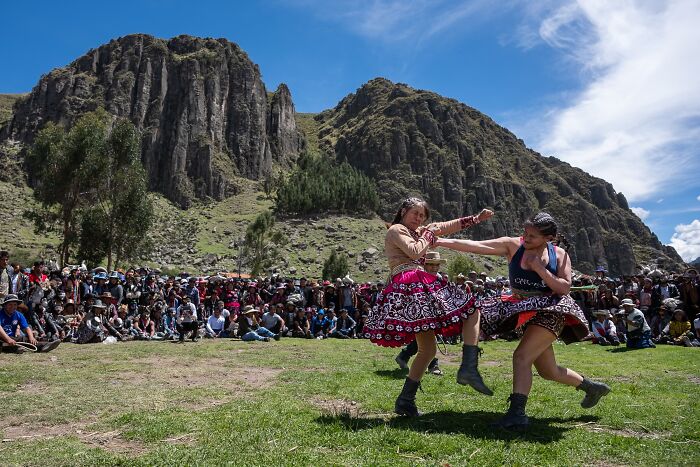 Women in traditional attire engage in a lively dance amidst a scenic mountain backdrop at a cultural event. Tokyo International Foto Awards.