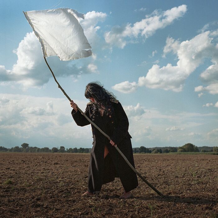 Person in a field holding a white flag under a cloudy sky, capturing a moment for the Tokyo International Foto Awards.