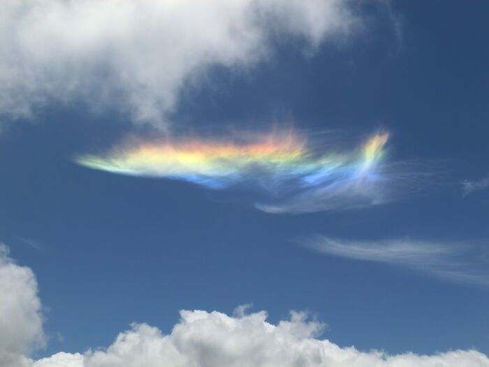 Rainbow cloud in blue sky, showcasing stunning natural phenomena above white fluffy clouds.