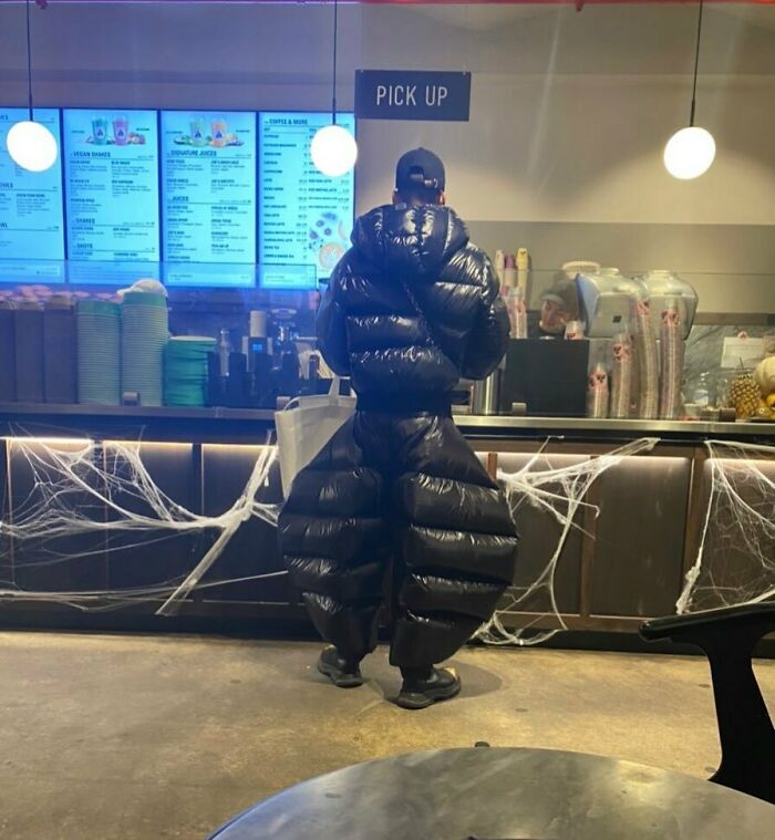 NYC local in a bold, puffy outfit at a cafe pick-up counter, showcasing experimental fashion.