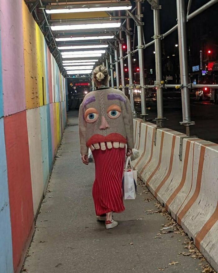 NYC local in vibrant outfit with animated face design walking at night, showcasing bold New York fashion.