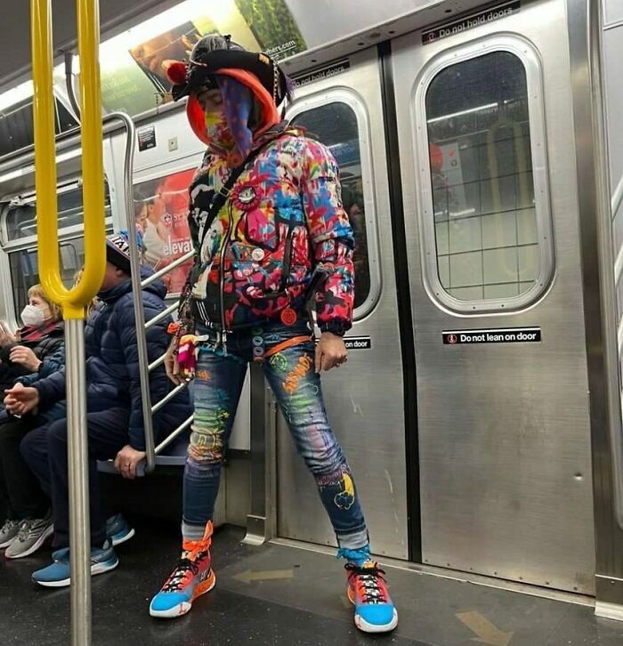 NYC local on subway in colorful, experimental fashion, wearing vibrant jacket, jeans, and sneakers.