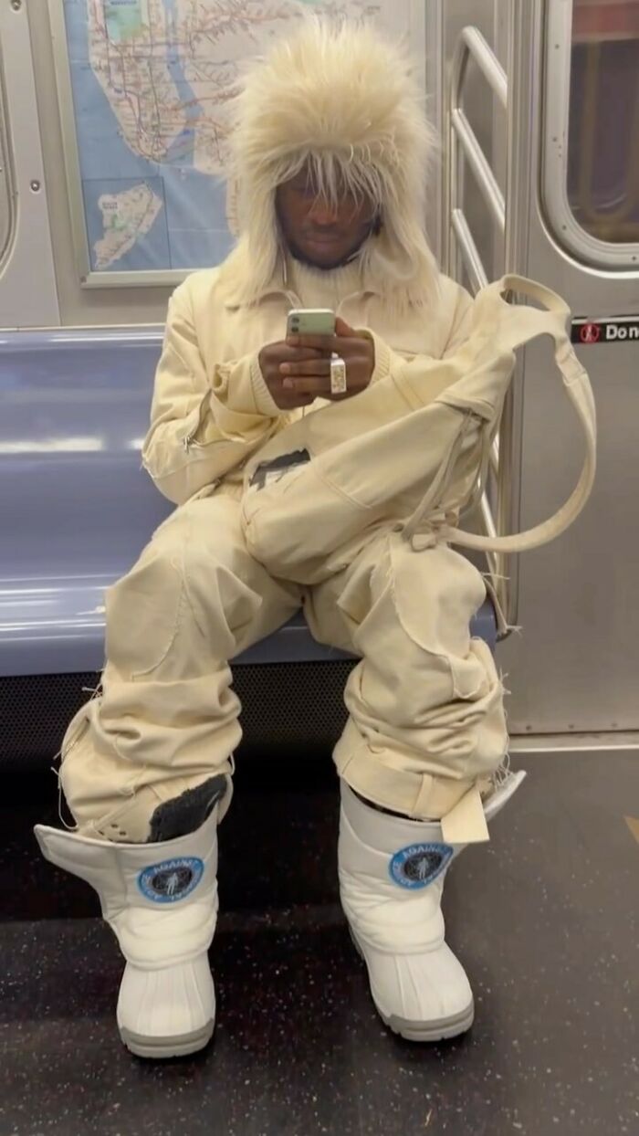 New York local in an experimental fashion outfit, wearing a fluffy hat and boots, seated in the subway.