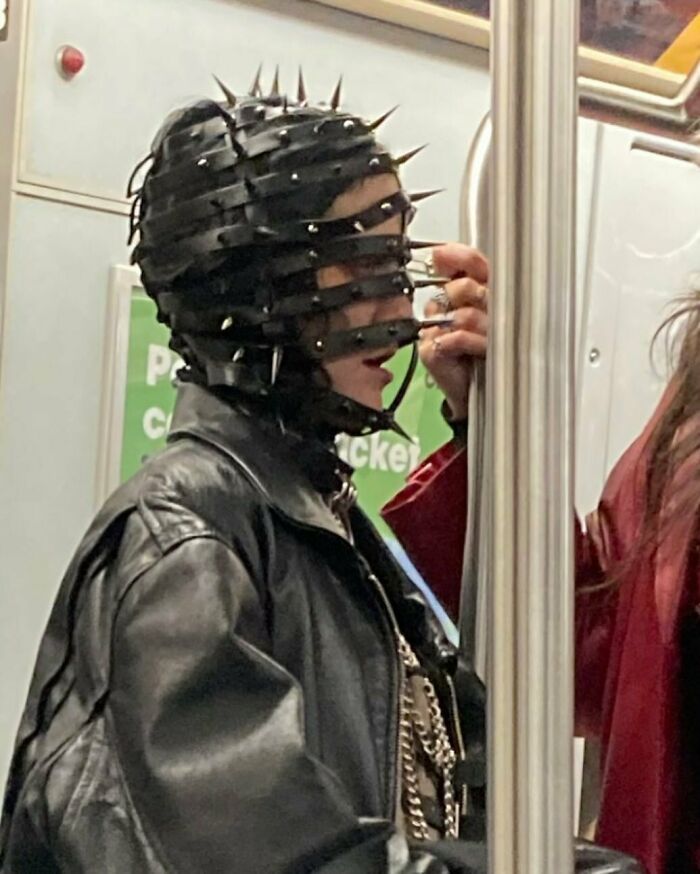 NYC local on subway wearing a spiked leather headpiece and black jacket, showcasing experimental fashion.