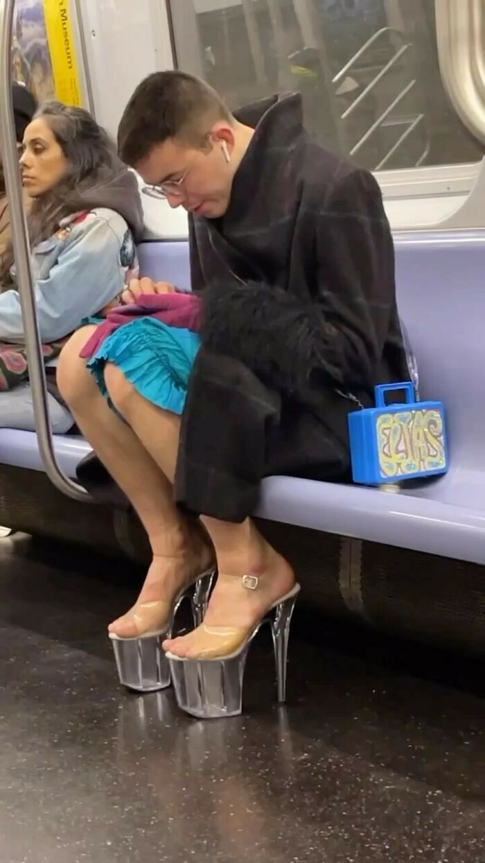 NYC local in subway wearing bold fashion: layered outfit with oversized coat and striking high platform heels.