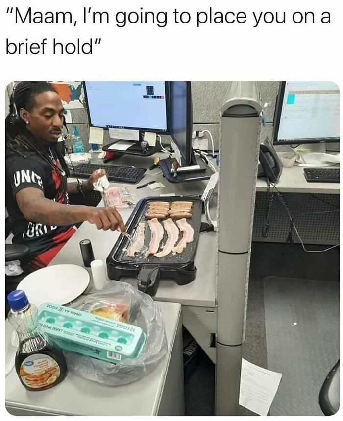 Office worker cooking bacon on a griddle at a desk, illustrating funny office meme.