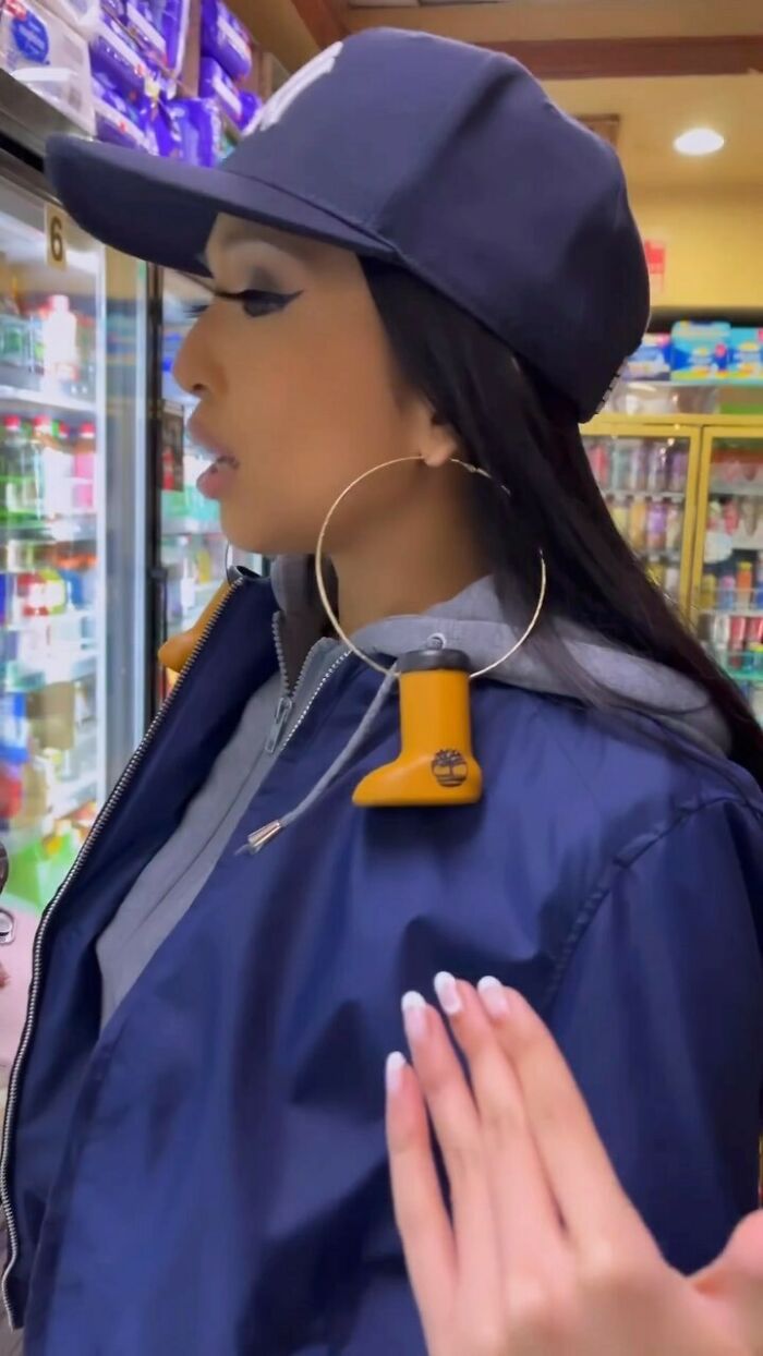 NYC local in a navy jacket and cap with bold hoop earrings featuring yellow boot pendants, showcasing unique fashion style.