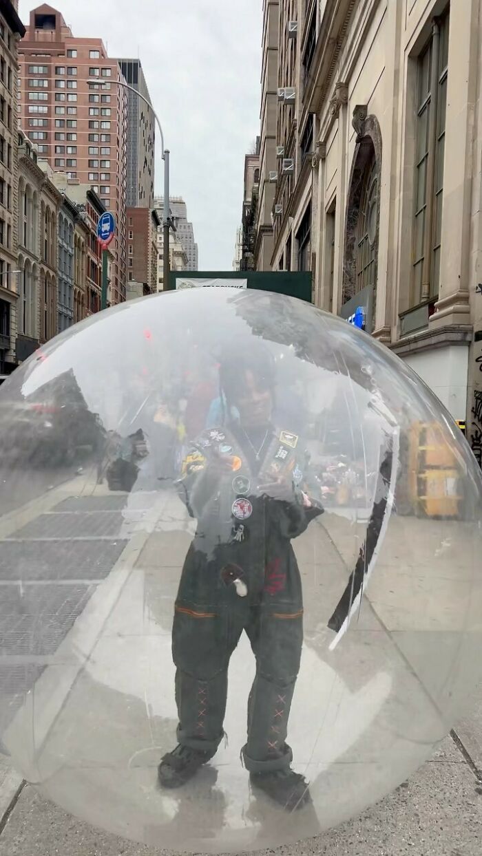 NYC local in a creative outfit standing inside a transparent bubble on a city street, showcasing unique New York fashion.