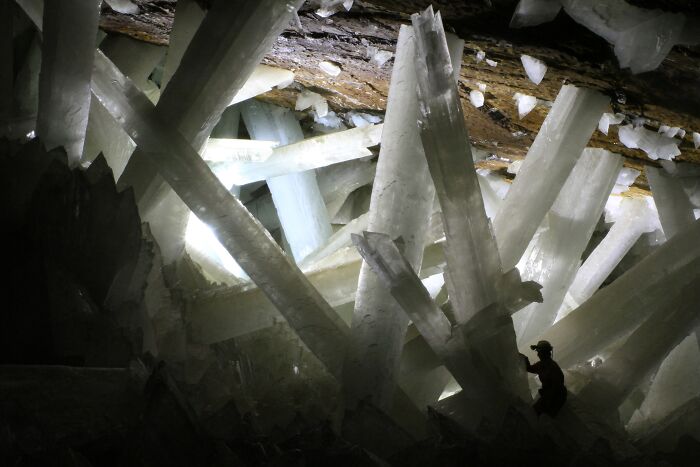 Person exploring a cave with giant crystals, showcasing strange natural phenomena.