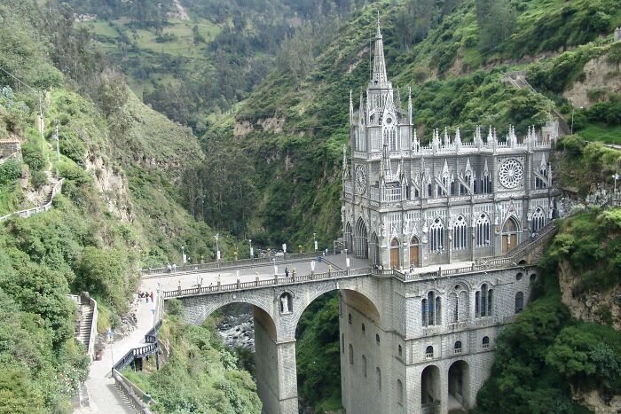 Gothic-style church on a bridge in a lush green gorge, showcasing fascinating architecture amidst natural beauty.