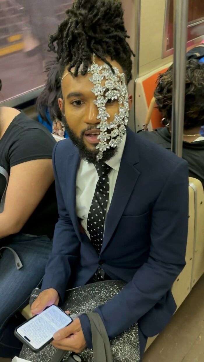 NYC local on subway wearing an expressive suit with crystal face accessory, showcasing bold fashion experimentation.