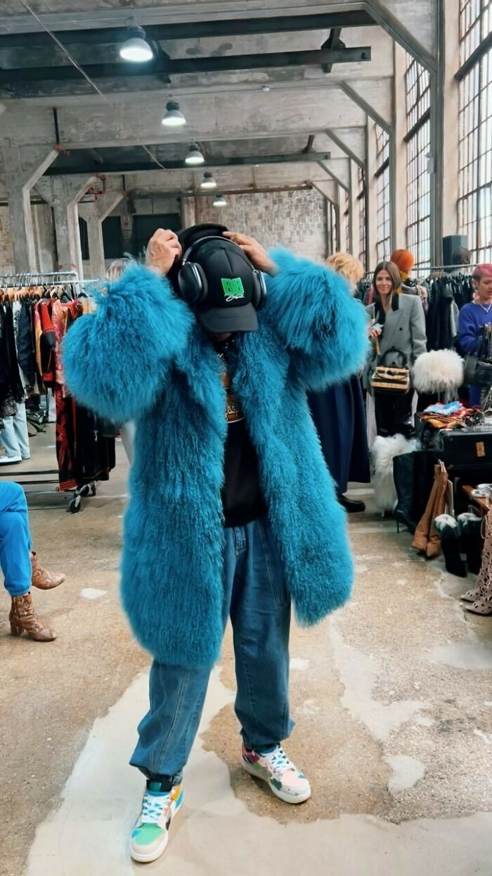 NYC local in a bold blue fur coat and colorful sneakers, showcasing experimental fashion at a market.