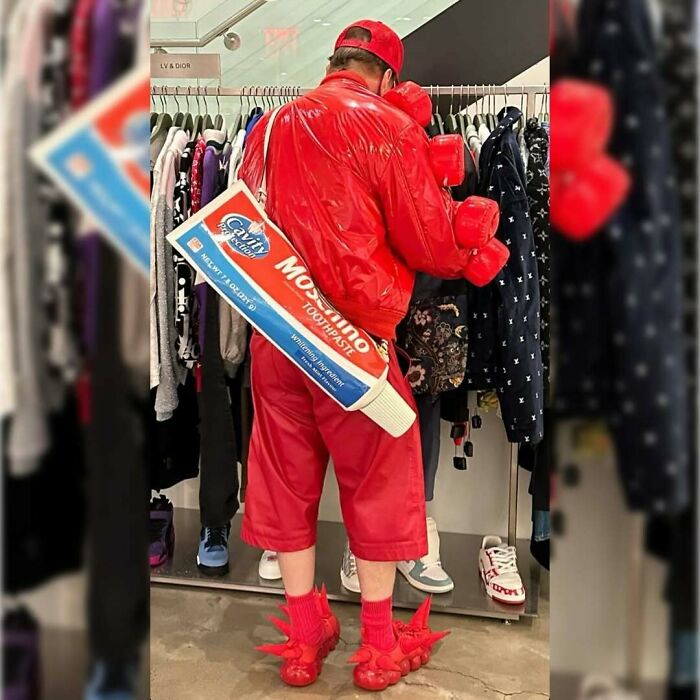 NYC local in bold red attire with a giant toothpaste-themed bag, showcasing experimental fashion at a clothing store.