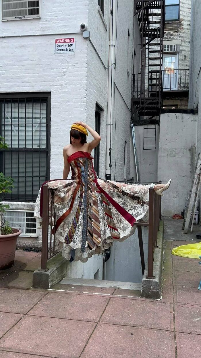 NYC local wearing an experimental fashion dress with colorful ties in an urban alleyway.